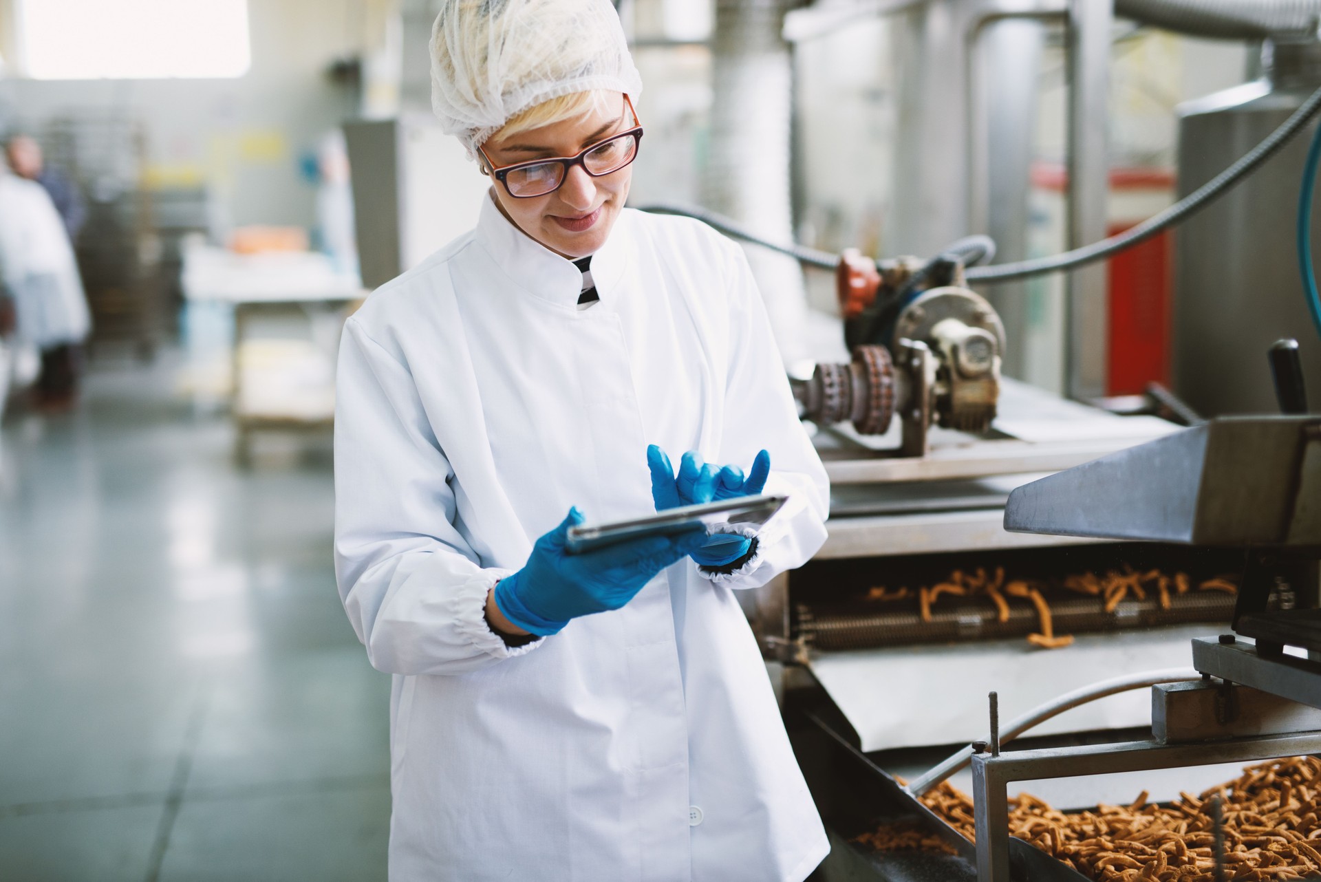 Young female worker in sterile clothes is checking quality of products in food factory.